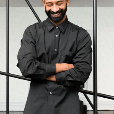 Photo of program faculty, Brendan Fernandes, looking down with arms folded, laughing