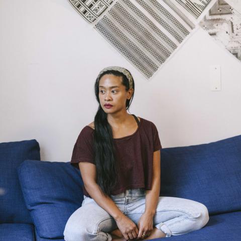 Photo of program faculty, Stephanie Comilang, sitting cross-legged on couch looking to her right