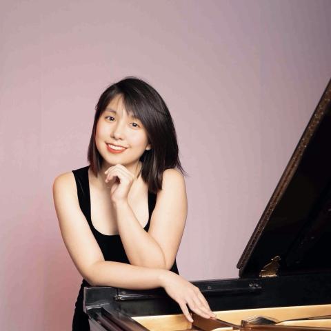 Woman leaning over piano smiling in black dress