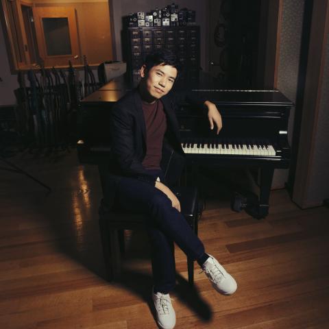 Man in black suit sat in front of piano looking at camera