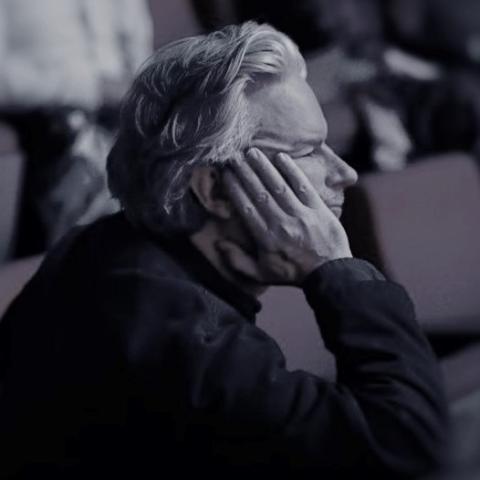 man in theatre looking off to the side with hand pressed against side of face
