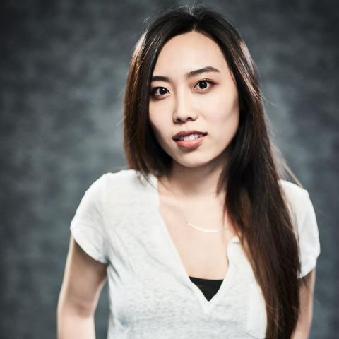 Woman in white t-shirt with hands behind back in pant pockets smiling at the camera