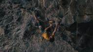 Man climbing on an overhang roof executing a challenging upside-down move with foot-hook.