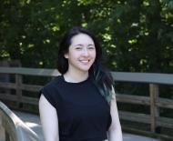 Smiling woman with dark hair posing by a wooden fence.