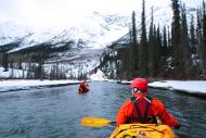 Kayakers on a river surrounded by snow and mountains