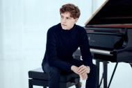 A man dressed in black is seated at a grand piano