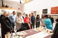 Guests gather around a table as a visual artists displays her work. 