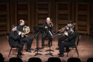 Chamber music group of 5 musicians on stage. Interplay Faculty and Participant Chamber Music Concert, 2025. L to R: Joel Brennan (trumpet), Tyrell Loster Peitzsche (horn), DJ Combs (bass trombone), Charlie Cao (trombone), and Fiona Shonik (trumpet)
