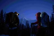 In a dark setting, a man and women with warm winter clothes, backpack, headlamp and climbing gear looking at each other, facing a snowy mountain 