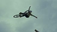 A fearless mann wearing a helmet taking a jump on his bike, spreading his arms like wings