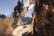Biker speeding on a mountain road with Tibetan prayer flags hanging between trees and rocks