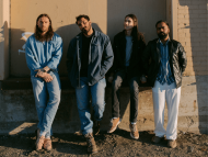 Four young men standing with a relax posture in front of a brick wall waring denim and 